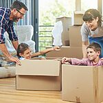 A Family Moving Into A New Home And Playing With Cardboard Boxes.