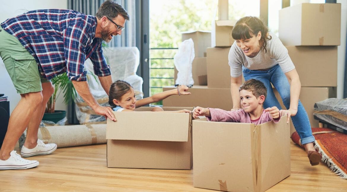 A Family Moving Into A New Home And Playing With Cardboard Boxes.