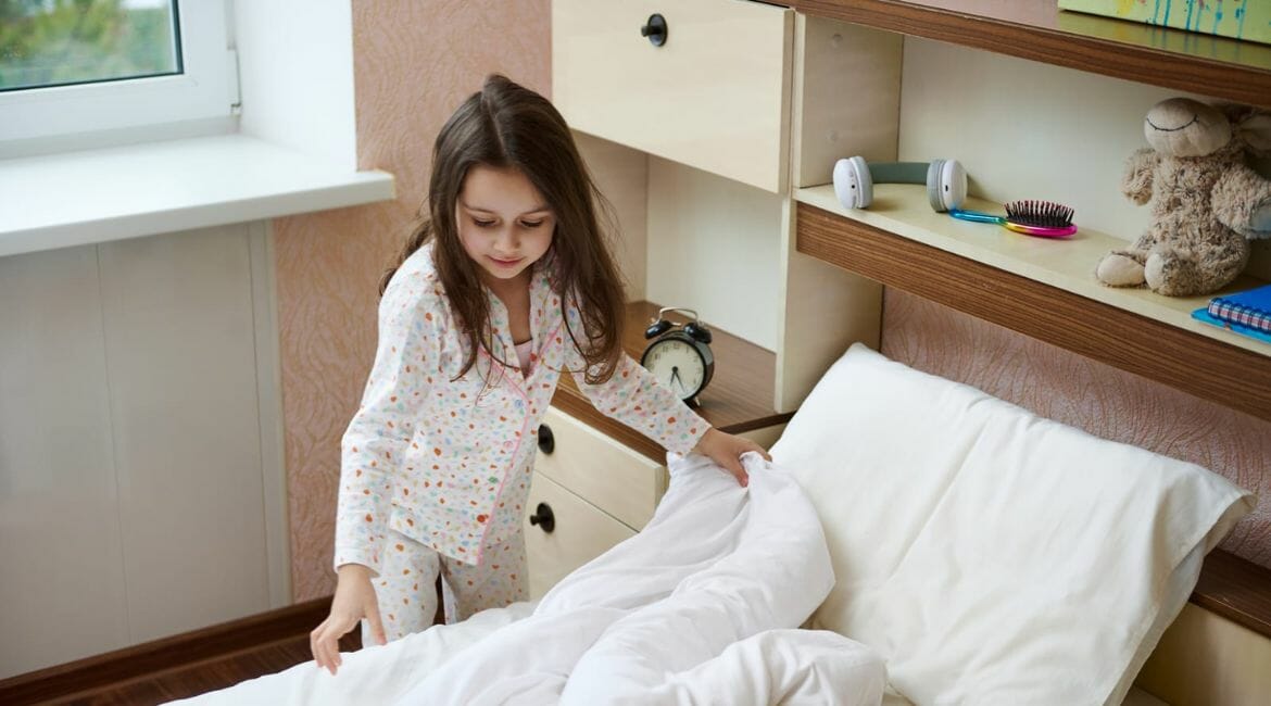 A Little Girl Is Putting A Blanket On Her Bed In Her Homeschool.