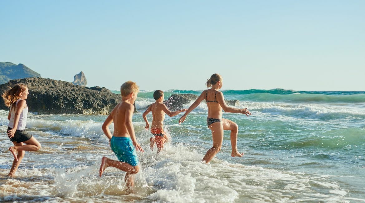 A Group Of Children Running And Having Fun In The Ocean During Homeschool Summer Break.