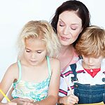 A Mother And Two Children Are Working On A Piece Of Paper.