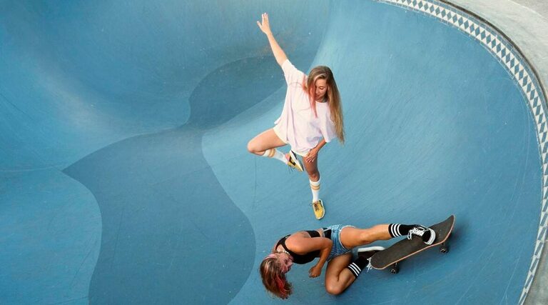 Two Women Skateboarding In A Skate Park.