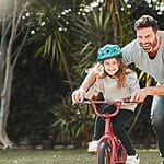 A Man And A Girl Riding A Bike In A Park.