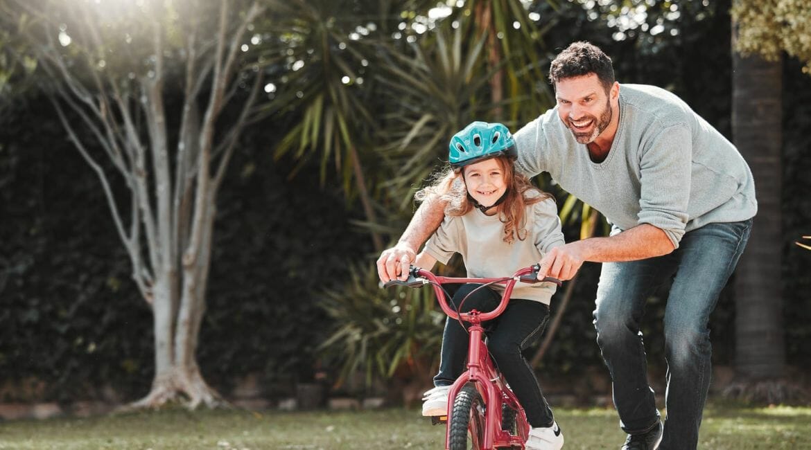 A Man And A Girl Riding A Bike In A Park.